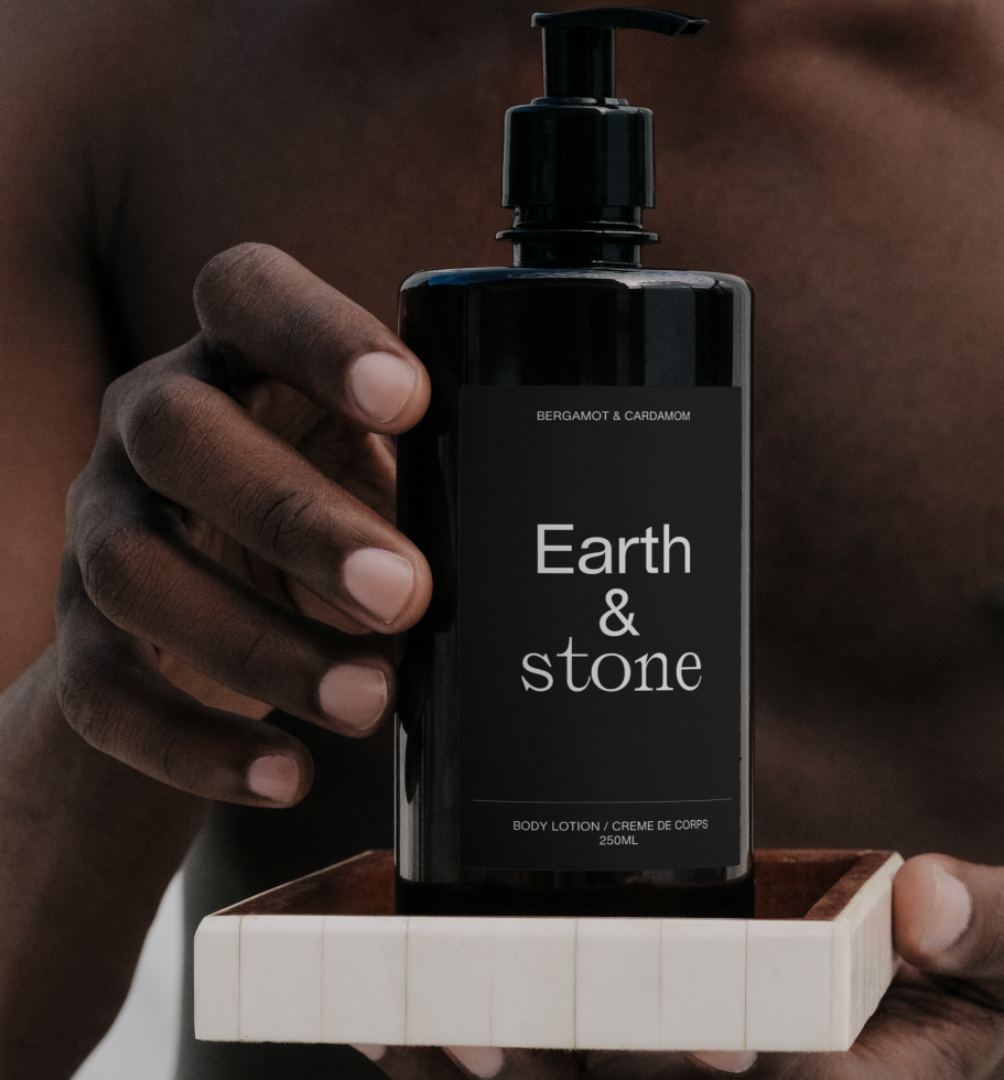 Product mockup of Earth & Stone body lotion held in hands against a dark background, ideal for beauty and skincare design presentations.